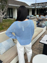 Person wearing a light blue sweater and white pants standing on a patio.