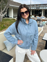 Woman wearing a light blue jacket and sunglasses outdoors.