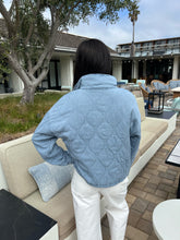 Person wearing a blue quilted jacket standing outdoors in a residential area.