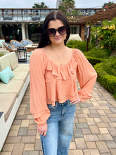 Woman wearing a peach blouse and blue jeans standing outdoors.