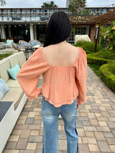 Person wearing a peach blouse and blue jeans standing in an outdoor setting with a building in the background.