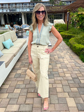 Woman in a light outfit standing on a patio with outdoor furniture and greenery.