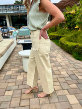Woman in a light green top and beige pants standing on a patio with outdoor furniture and plants in the background.
