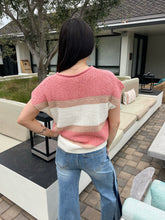 Person wearing a pink and white striped sweater and blue jeans standing in an outdoor setting.