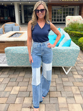 Woman in a blue top and patchwork jeans standing in front of outdoor furniture.