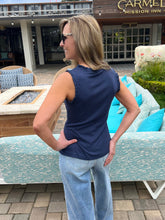 Woman in a blue sleeveless top and jeans standing in front of a patio with outdoor furniture.