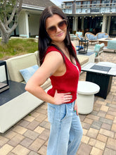 Woman in a red top and light blue jeans standing outdoors on a patio.