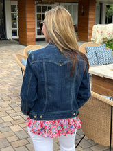 Person wearing a denim jacket and floral blouse standing outdoors.