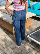 Person wearing a striped shirt and blue jeans standing on a patio.