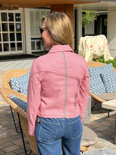 Woman wearing a red checkered jacket and blue jeans standing outdoors.