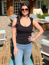 Woman wearing a black tank top and sunglasses outdoors on a patio.
