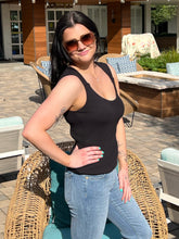 Woman in black tank top and jeans standing outdoors on a patio.
