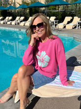 Woman in pink sweater with a floral design sitting by a pool.