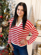 A woman wearing a red and white striped knit sweater with a V-neck and long sleeves, standing in front of a decorated Christmas tree and holiday decor.