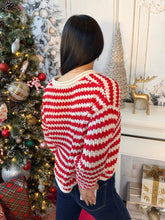 A woman viewed from behind wearing a red and white striped knit sweater, standing in a decorated holiday room next to a Christmas tree.