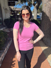 Woman wearing a lilac shirt and sunglasses standing outdoors on a sunny day.