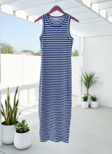 Blue and white striped dress hanging on a rack with plants and a white railing in the background.
