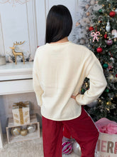 Woman standing in front of a Christmas tree wearing a white sweater showing the back view and wearing red track pants.