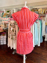 Mannequin wearing a red and white striped dress in a store setting with racks of clothes in the background.