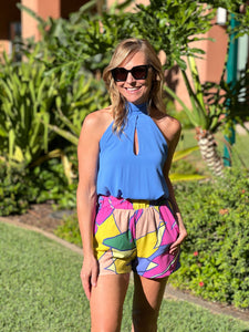 Picture of women wearing blue halter top tucked into colorful shorts. 