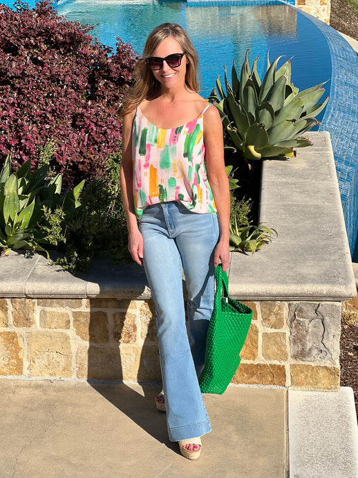 Women posing wearing a colorful tank top, flare jeans and a green purse.