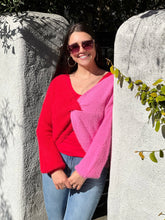 Women posing against a wall in a pink and red sweater, showing front view.