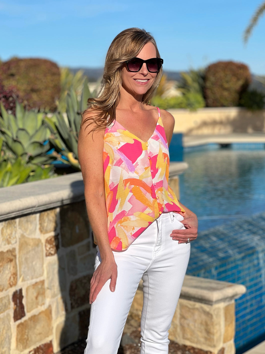 Women posing near a pool wearing a bright colored tank top, showing front view.